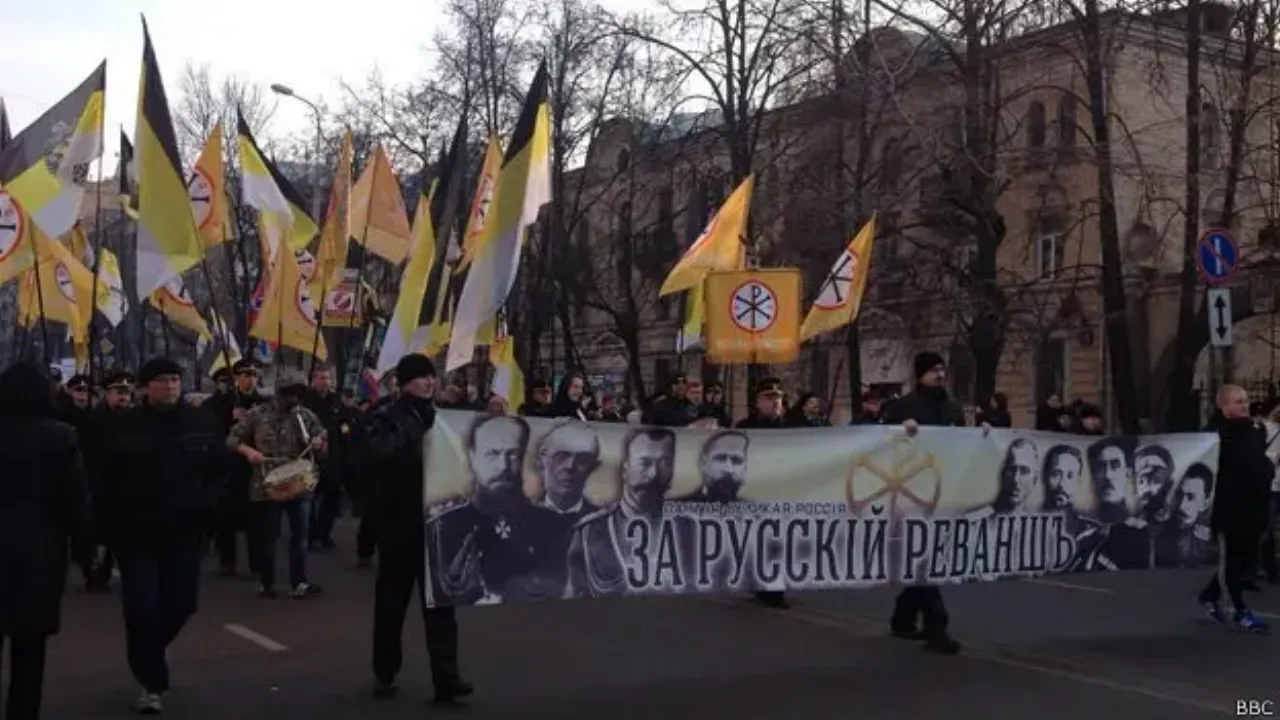 A march under black-yellow-white imperial flags, led by a banner reading “ЗА РУССКИЙ РЕВАНШЪ” with portraits on it.