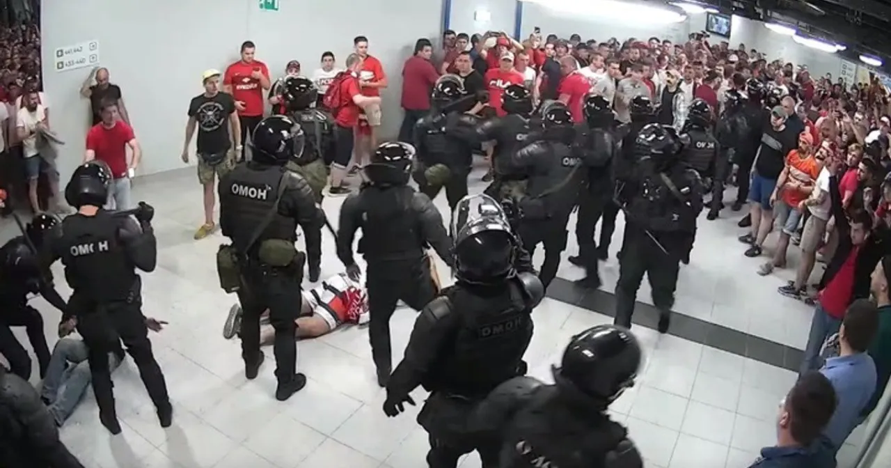 Helmeted OMON push a crowd of fans in red through an underpass; one person lies on the floor.